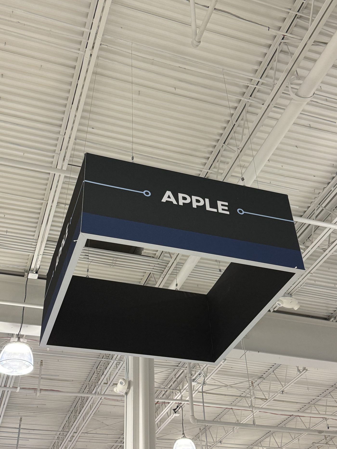 Square hanging fabric sign suspended from a warehouse ceiling, printed for an Apple retail display